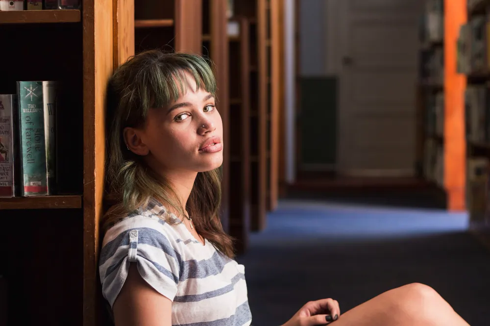 Young person in a contemplative pose against a library bookshelf, illustrating the reflective work of counselling for young people in London.