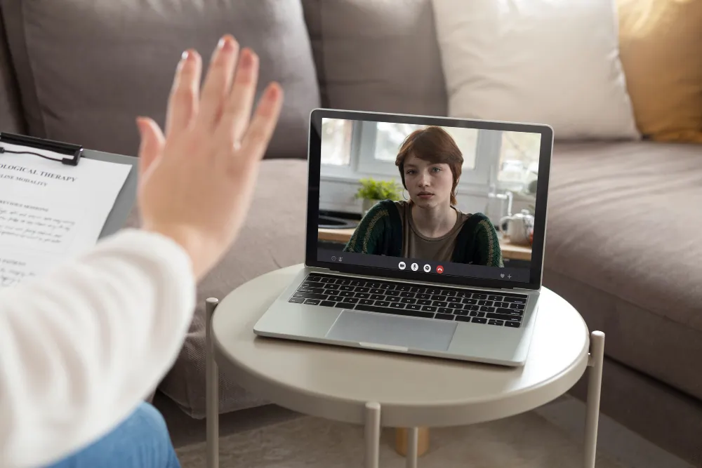 A UKCP psychotherapist conducting an online video therapy session with a client visible on the laptop screen.