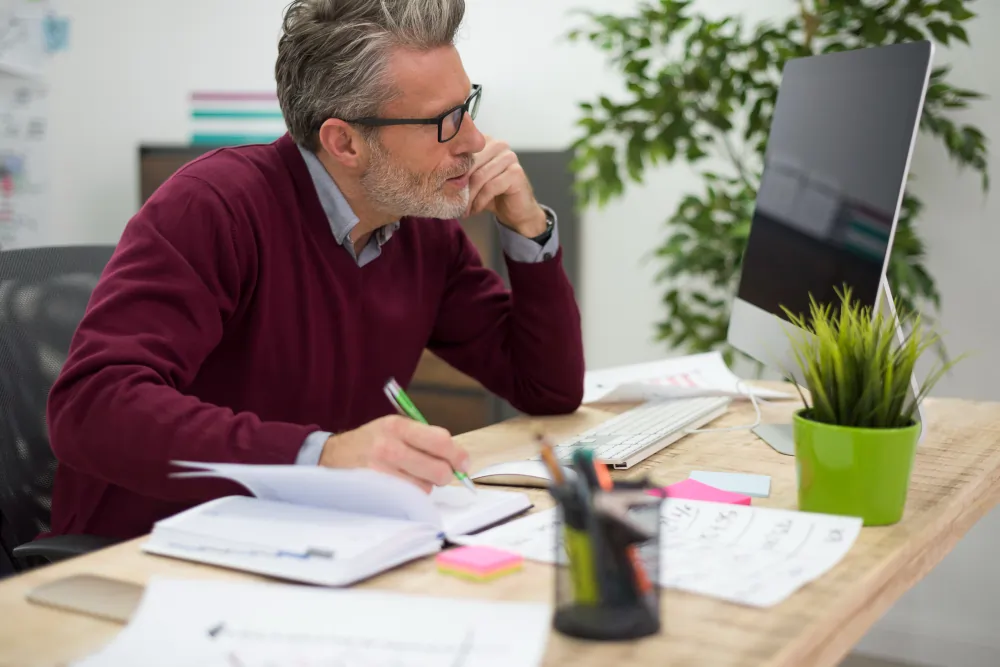 A professional planning their work thoughtfully at an organised desk during focused, deep-work time.