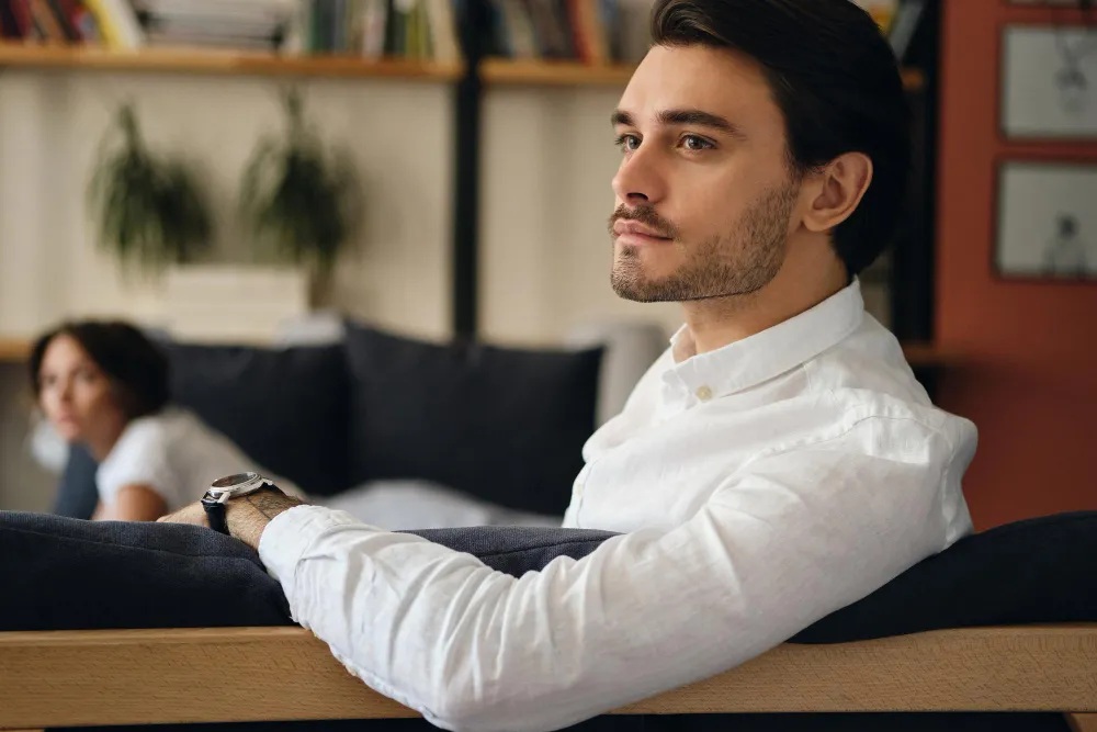 Adult professional man sitting on an office sofa, attention drifting elsewhere. The high-masking presentation of adult ADHD.