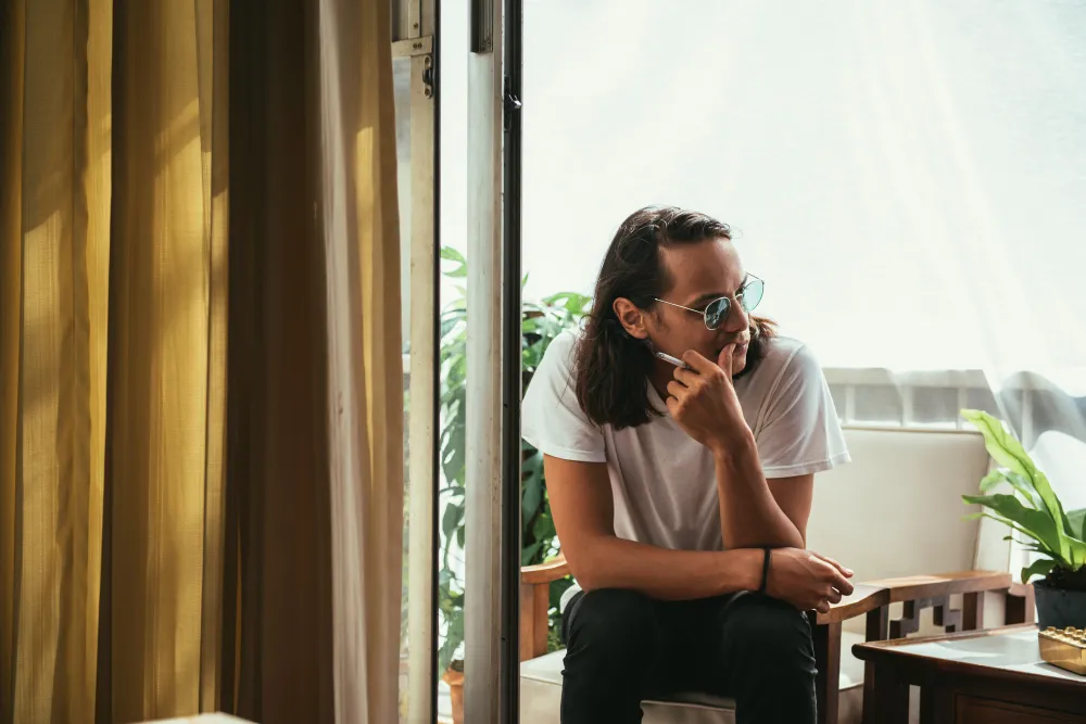An adult sitting quietly by a sunlit window, looking calm and reflective.